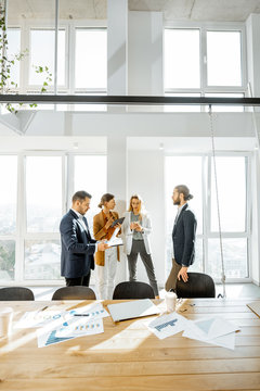 Group Of Young Business People Working And Having Some Discussion In The Spacious Meeting Room With Large Table And Office Supplies On The Foreground