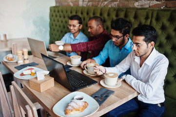Fototapeta na wymiar Group of four south asian men's posed at business meeting in cafe. Indians work with laptops together using various gadgets, having conversation and drink coffee.