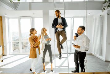 Group of a young creative office employees having some informal discussion, while standing together in the bright meeting room with large windows