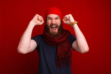 Angry winner, bearded guy wearing warm clothes and celebrating with arms up and screaming at camera