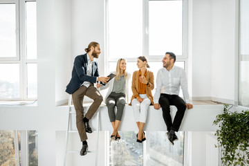 Fototapeta premium Group of a young creative office employees having some informal discussion, while standing in the two-level bright meeting room with large windows
