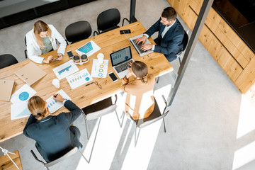 Business people working with computers and some printed statistics at the wooden table in the...