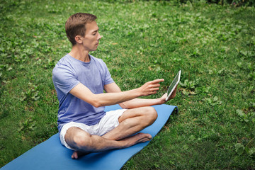Young attractive white man learns to meditate in the park in front of a laptop.