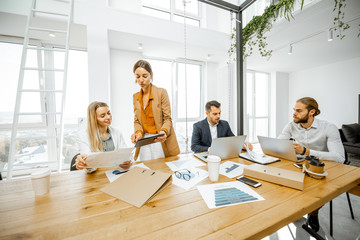 Group of a young office employees dressed casually in the suits having some office work at the large meeting table in the bright office