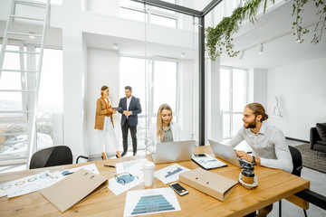 Group of a young office employees dressed casually in the suits having some office work in the bright meeting room, wide view on the spacious room