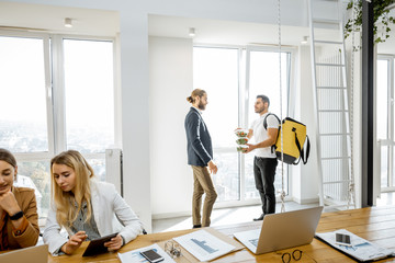 Courier delivering healthy business lunches with thermal bag for the office employees, happy businessman taking salads in the white office