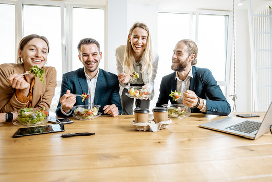 Group of a young office workers eating salads and drinking coffee at the modern office canteen. Concept of a healthy takeaway food on the work
