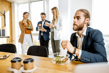 Group of a young office workers eating salads and drinking coffee at the modern office canteen. Concept of a healthy takeaway food on the work