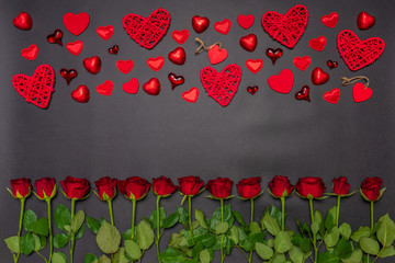 Border made of fresh red rose flowers, hearts and sweets on black background. Floral composition, greeting card for holiday event. Love, romance or Valentine's day concept. Flat lay, top view, mock up