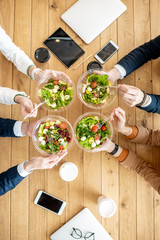 Office workers during a business lunch with healthy salads and coffee cups, view from above on the...