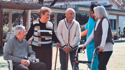 African nurse talking to two elderly retired couples outdoor in the rehab hospital garden. Happiness, rehabilitation and retirement concept