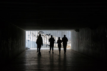 People walking through a dark underpass with glowing end, underground passage, blurred people silhouettes 