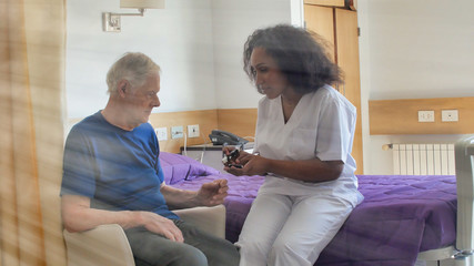 Fototapeta premium Afrykańska lekarka odwiedzająca starszego mężczyznę w łóżku szpitalnym. Koncepcja rehabilitacji i emerytury