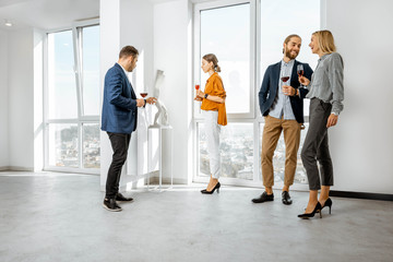 Young elegantly dressed people meeting in the white hallway or showrroom of the modern art museum, drinking wine and looking on the sculpture