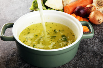 Broth with carrots, onions various fresh vegetables in a pot - colorful fresh clear spring soup. Rural kitchen scenery vegetarian bouillon stock
