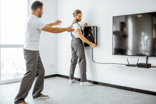 Two Professional Workmen In Workwear Installing Luxury Audio System In The White Living Room. Home Appliances Installation Concept