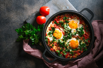 Shakshuka with eggs, tomato, and parsley in a iron pan. Top view copy space