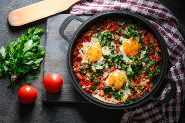 Shakshuka with eggs, tomato, and parsley in a iron pan. Top view copy space