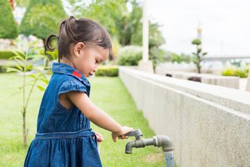 Cute asian little girl is trying to open tap water faucet in the park, concept of learning by playing for toddler development.