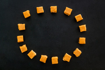 Caramel pieces - round lined with sweets - on black background top view mockup copy space
