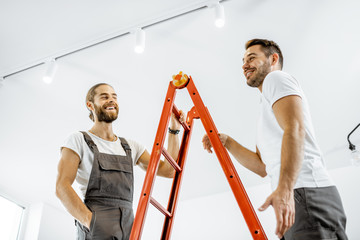 Two handsome workmen in uniform talking on the ladder during some repairment at home