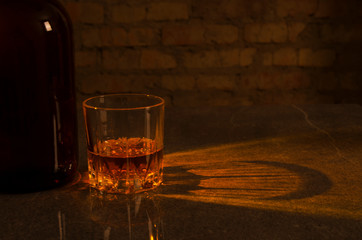 Glass of alcoholic drink, bottle of whiskey on the bar counter against old brick wall