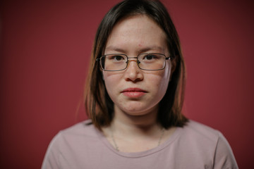 Portrait of a plain woman in glasses against a red wall.