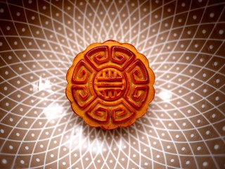 Top view photo of a mooncake with geometric ornament in a chinaware bowl with Oriental pattern. Traditional Chinese pastry for Mid-Autumn Festival.