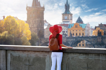 Elegante Touristin mit rotem Hut und Rucksack genießt die Aussicht auf die Karlsbrücke in Prag,...