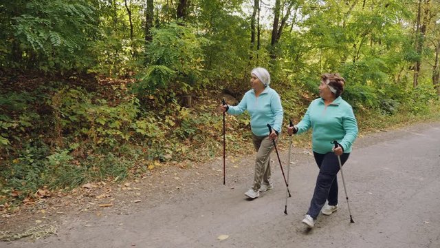Elderly senior women practicing Nordic walking outdoors, healthy lifestyles in old age. Women walk along the road. Slow-motion 4k video