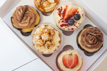 Box of assorted cupcakes with cream cheese vanilla and chocolate frosting, fresh strawberries, raspberries, blueberries and popcorn decoration. 