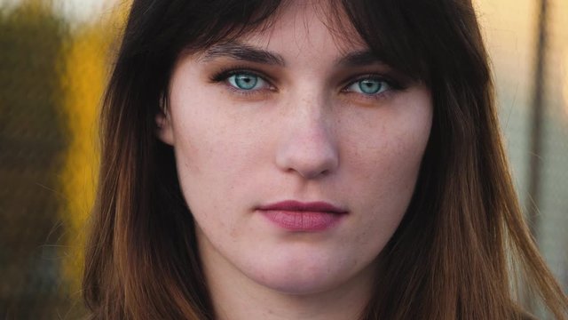 Close up portrait of woman with beautiful blue eyes, long brown hair look at camera. With serious face, natural skin and less make up.