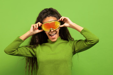 African-american young brunette woman's portrait in ski mask on green studio background. Concept of...