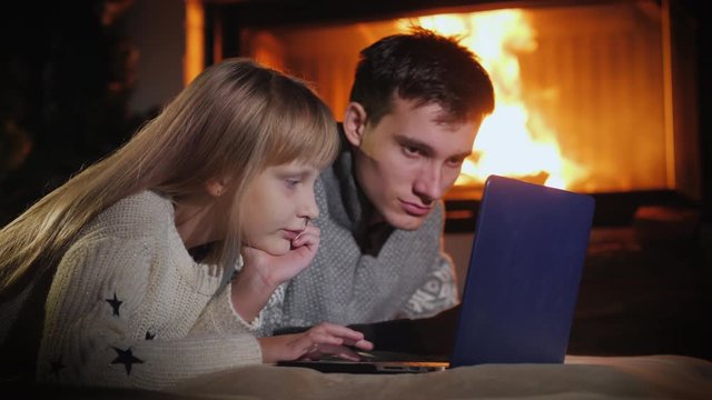 Children play together on a laptop, lie on the floor near the fireplace