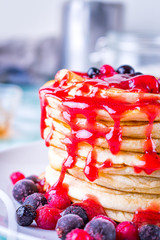 Pancakes with red fruits stacked with raspberry jam on a white plate.