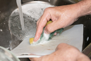 Fregando con estropajo tabla de cortar de cocina mientras el agua corre