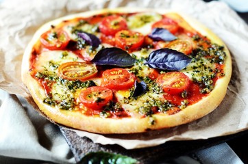 Pizza margarita with pesto on a dark wooden background
