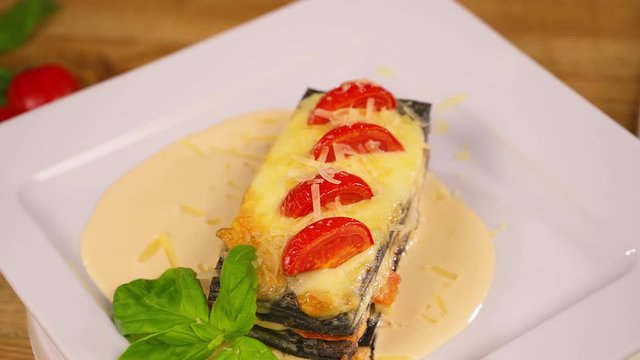Italian black lasagna with salmon and mushrooms serving on white plate in restaurant