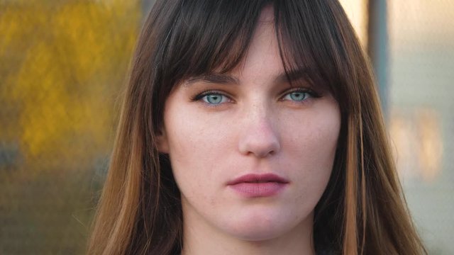 Close up portrait of woman with beautiful blue eyes, long brown hair look at camera. With serious face, natural skin and less make up.