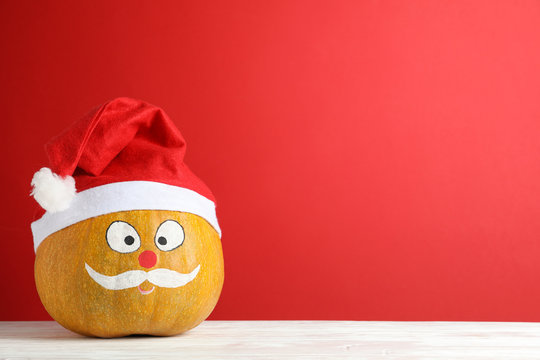 Pumpkin with mustache and red Santa hat against red background, copy space