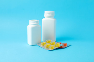 White medical bottles and different pills in blister packs on blue background, space for text
