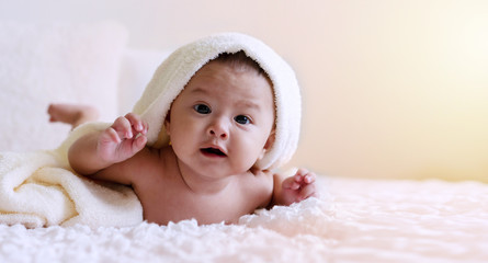 Cheerful cute baby looking at camera under white blanket looking at something. Innocence baby crawling on white bed with towel on his head at home.