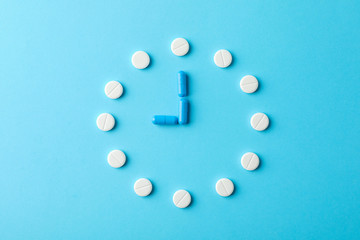 Clock made of pills on blue background, top view and space for text