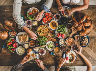 Turkish breakfast. Flat-lay of Turkish family eating traditional pastries, vegetables, greens, cheeses, fried eggs, jams and tea in copper pot and tulip glasses over rustic wooden background, top view