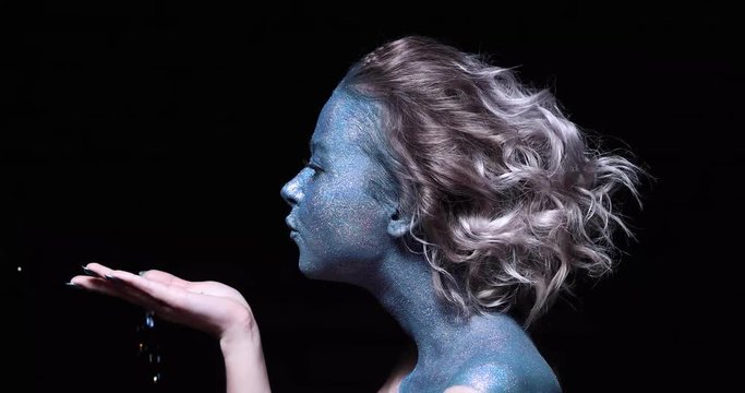 close-up of a girl with a blue face in sparkles against a black wall