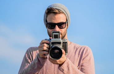 Obraz premium Photojournalist concept. Hipster reporter taking photo. Manual settings. Travel blogger. Professional photographer. Handsome photographer guy retro camera. Guy photographer outdoors sky background