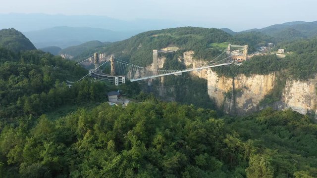 Approaching aerial view of stunning glass suspension bridge in Zhangjiajie, spanning 430 meters across beautiful mountain valley in central China