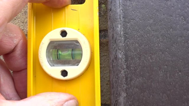 Slow motion, close POV shot of a man&rsquo;s hands checking vertical straightness of an upright with a spirit level / bubble level.
