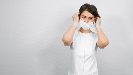 beautiful woman beautician puts on white protection mask standing against medical center wall close view