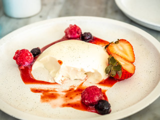 Bitten panna cotta topping with strawberry, blueberry and raspberry with jam in white dish